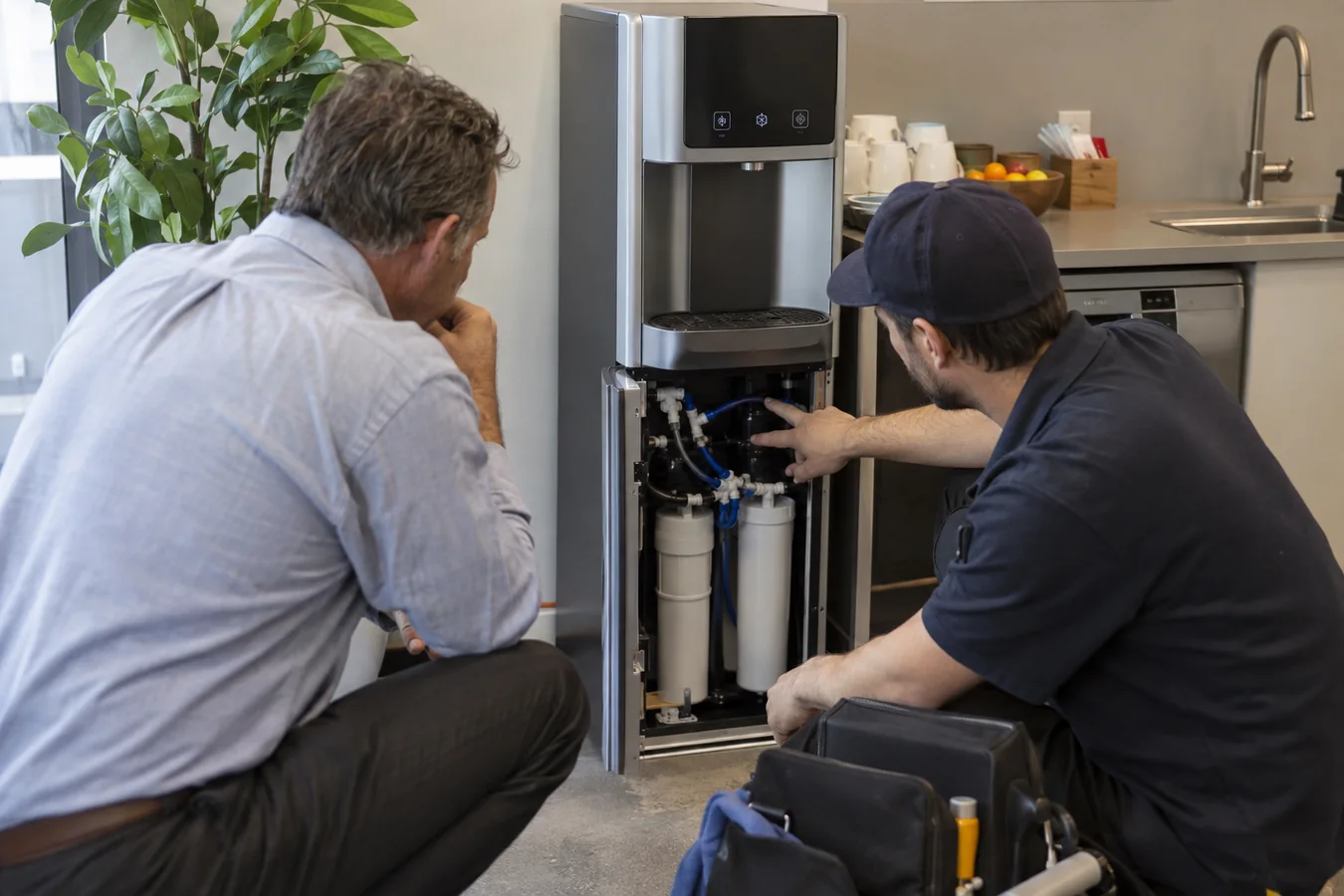 Facilities manager inspecting a bottleless office water cooler with a service technician